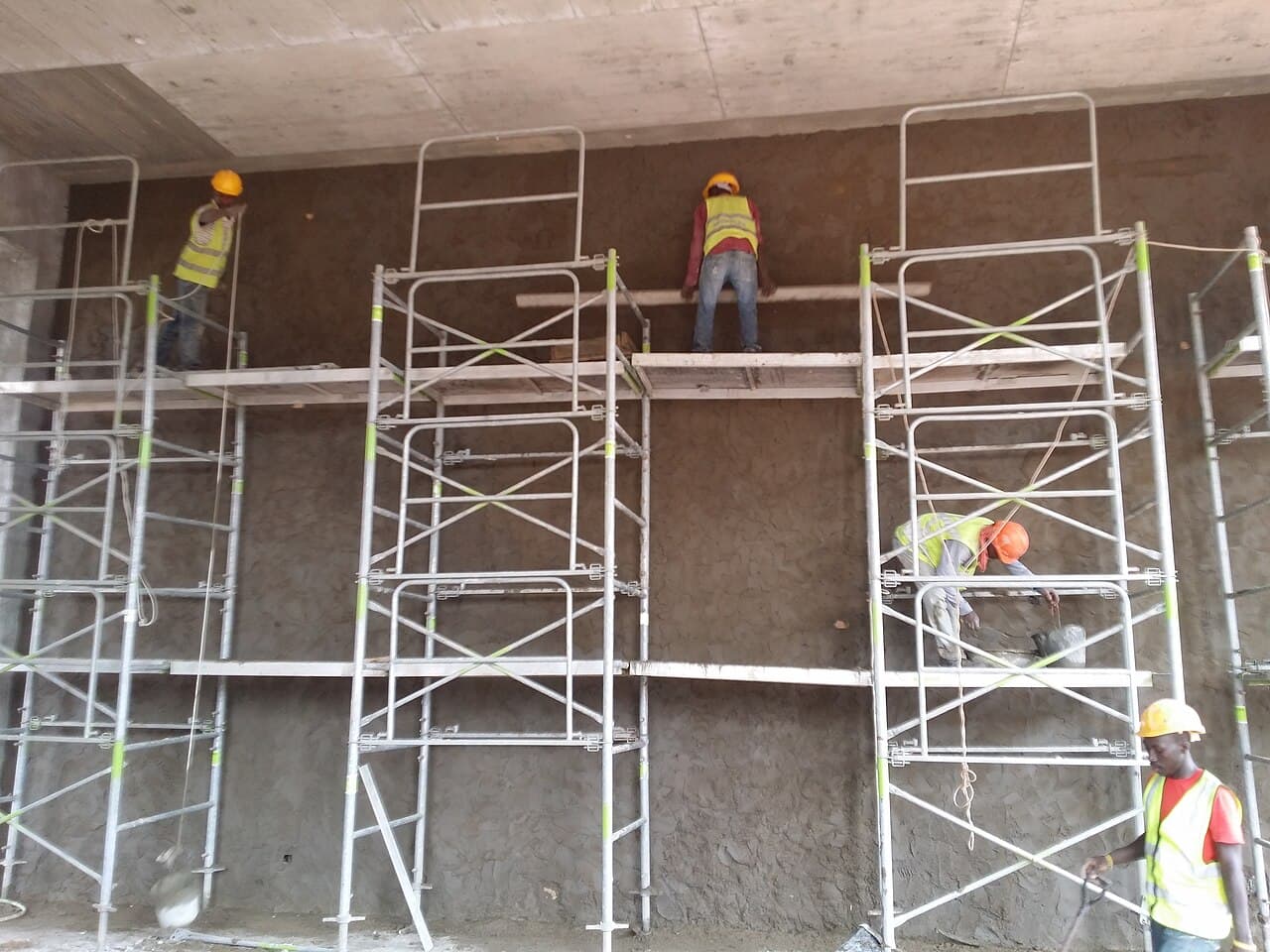 A crew plastering a wall from scaffolding on a building site.